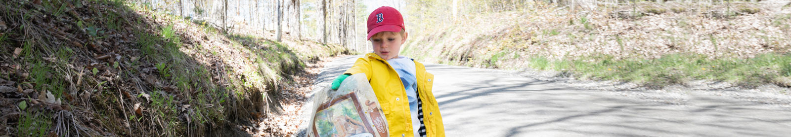 Photo of a little boy wearing a yellow rain coat and holding litter he picked up off the ground