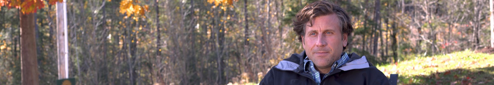 Man outside with trees and fall landscape in background