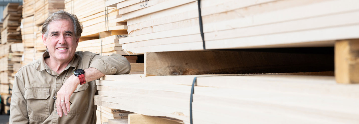 Photo of man leaning has arm on a stack of lumber