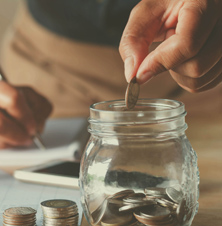 Person dropping spare change into glass jar for savings