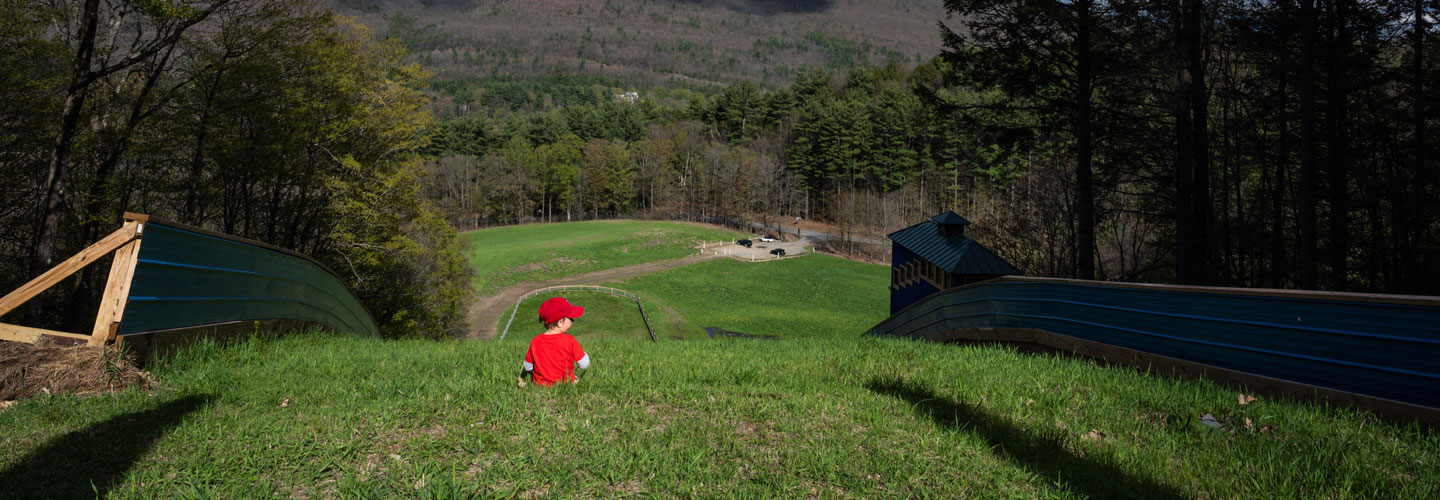 Image of little boy wearing a red t-shirt and baseball cap, sitting in the grass