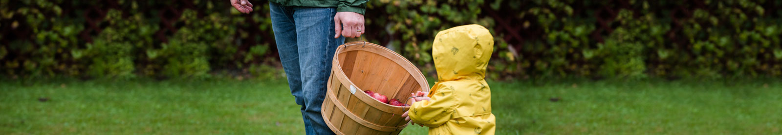 Photo of a parent and child, holding a wooden bushel of apples at an orchard