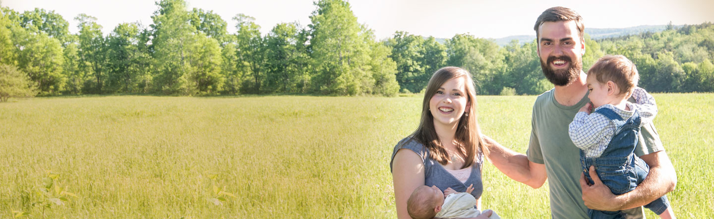 Happy family standing in a field, with mother holding infant and father holding toddler