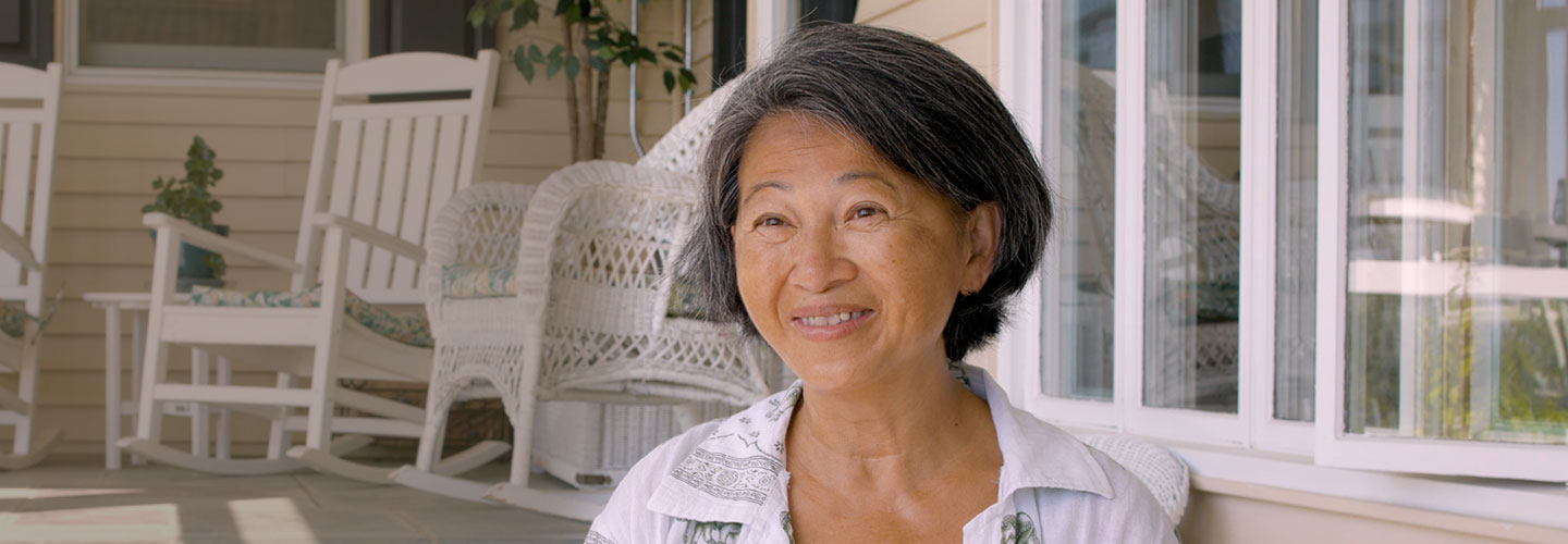 Smiling woman on a porch with white wicker chair and white rocking chair