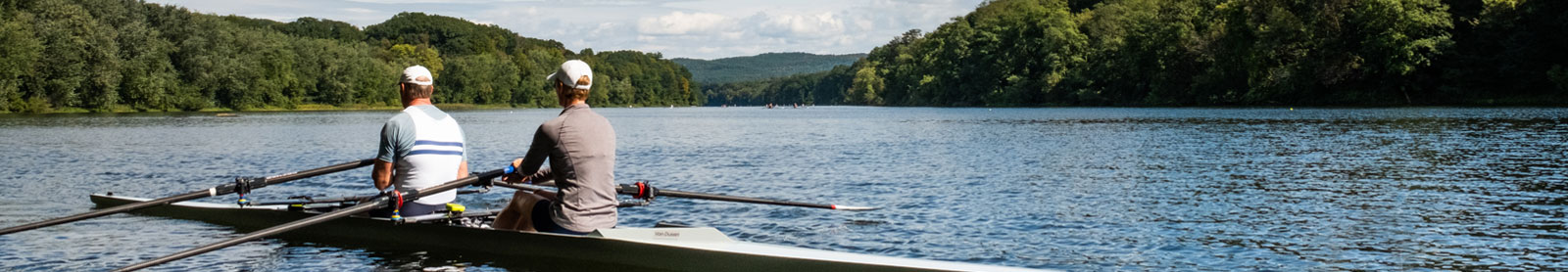 scenic photo of two men rowing small boat on lake with mountains in background
