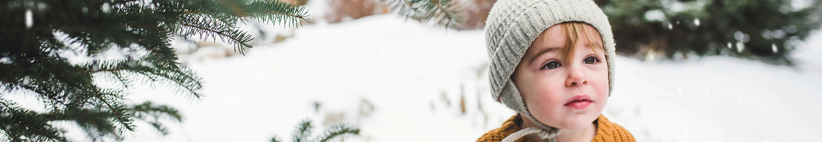 photo of a little toddler boy wearing a knit cap outside with a snowy background behind him