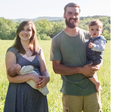 Smiling young family holding baby and toddler in front of mountain view