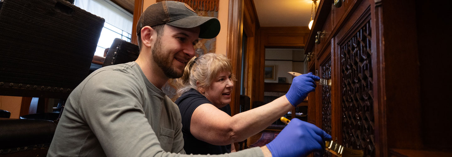 Two BS&L employees shown volunteering and wearing blue latex gloves and using small paint brushes