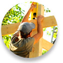 cropped photo of carpenter wearing baseball cap and holding a level against wooden beams