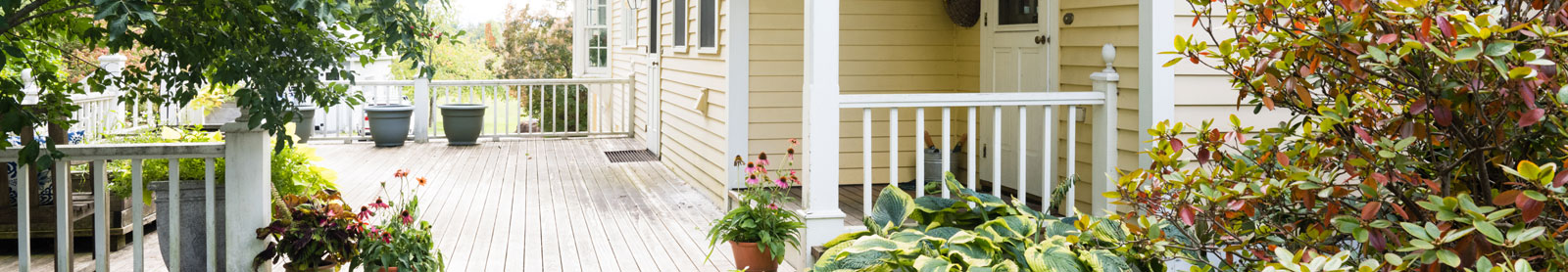 Beautiful deck with white railings and lush garden in front of a pale yellow house