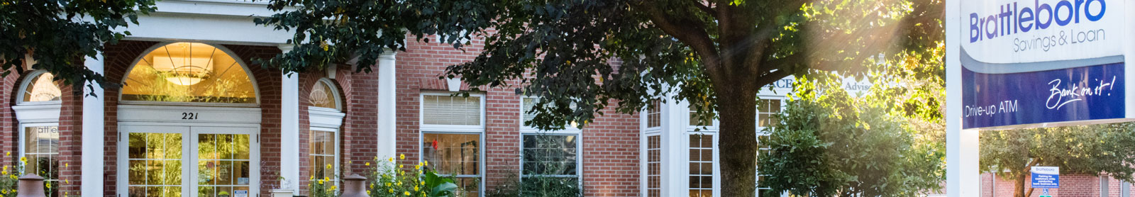 Cropped photo of BS&L's main office, a  brick building with trees in front