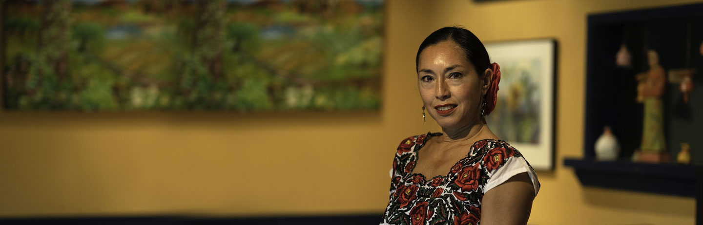 Attractive woman standing inside with a large painting on a yellow wall behind her