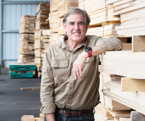 Man standing with arm leaning on tall stack of lumber