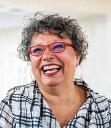 Smiling woman with curly hair wearing glasses and hoop earrings