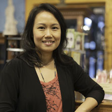 Smiling woman shop owner, standing with her arm resting on the counter