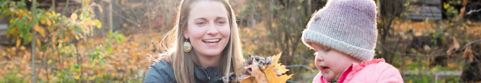 Young mother with toddler girl playing outside with fall leaves