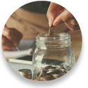 Close up photo of person's hand dropping change into a glass jar for savings