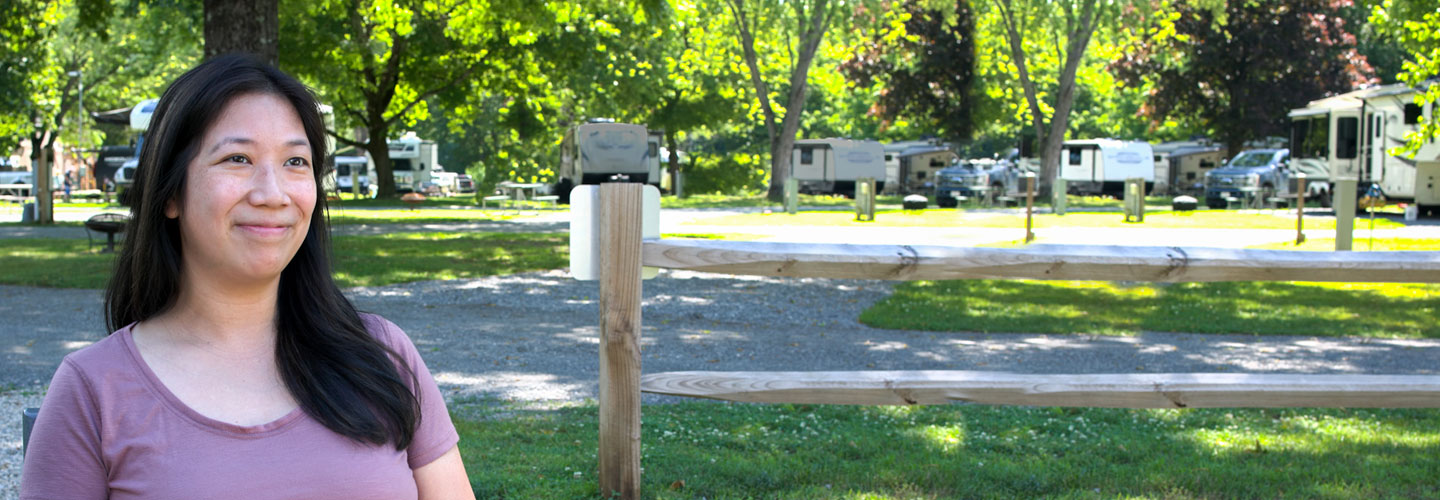 Photo of young woman sitting outside with a campground behind her
