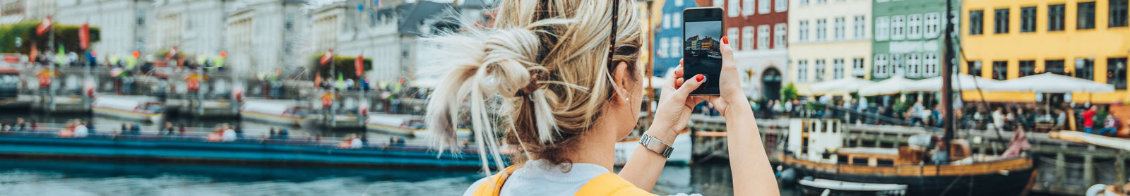Woman holding her phone and taking a photo on vacation in a beautiful European waterfront destination