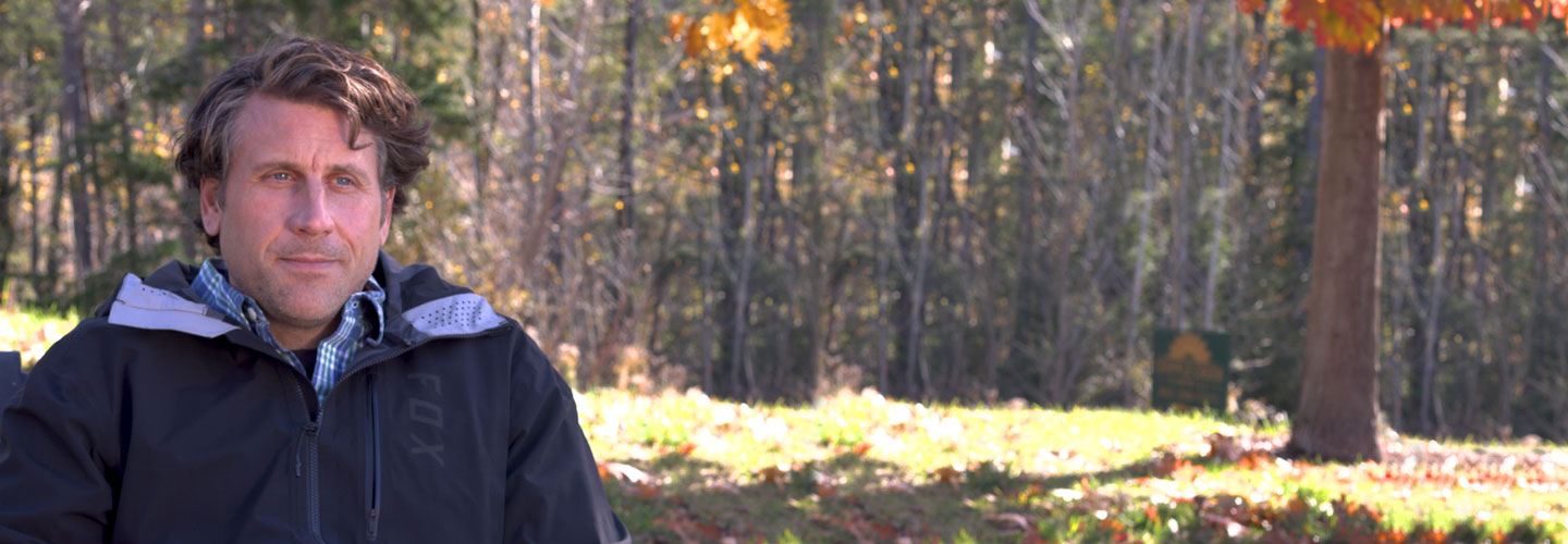 Man with thoughtful expression outside with grassy landscape and trees in background
