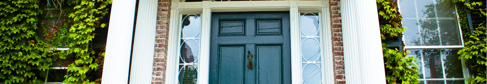Cropped photo of blue-green colored front door with white columns and brick facade covered by ivy