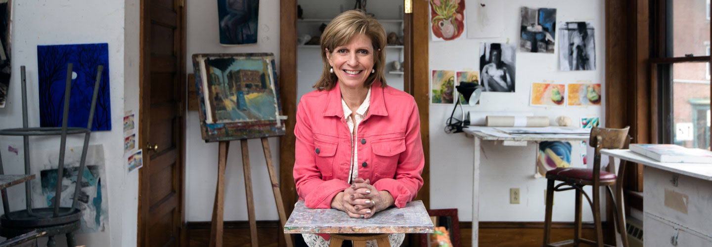 Woman artist sitting in painting studio wearing hot pink jacket
