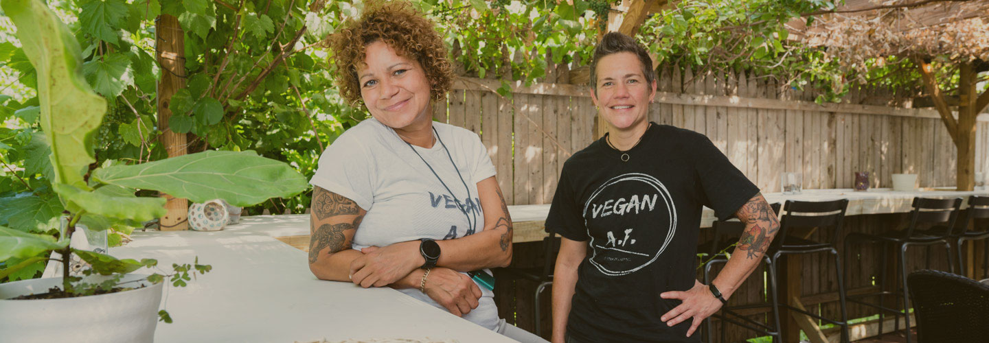 Two women standing outside in garden setting with wooden fence behind them