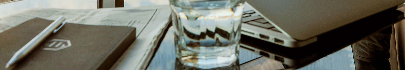 Cropped photo of desk with pen on leather notebook glass of water and partially closed laptop