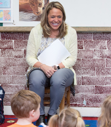Smiling woman sitting in chair with group of school children
