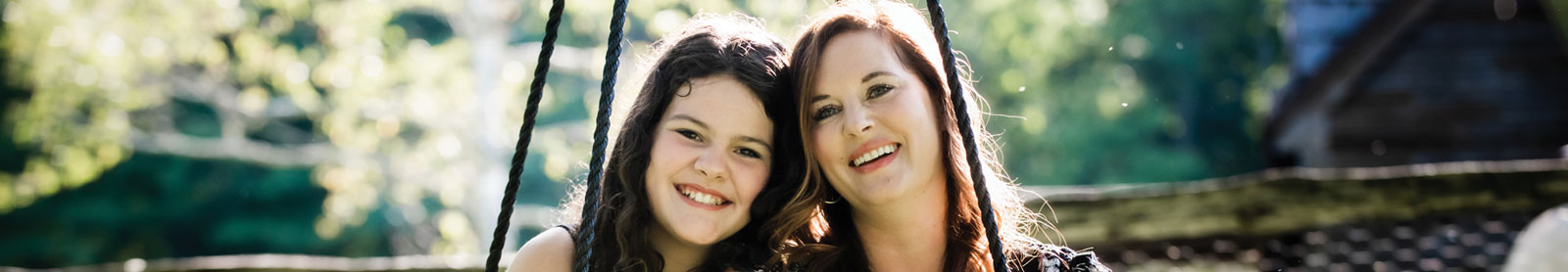 Smiling mother and teenage daughter sitting outside together on swing