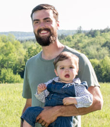 happy smiling dad holding baby standing outside with scenic mountains and trees in background