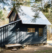 Dark gray tiny home with metal roof and stones around foundation